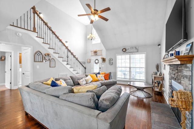 living room featuring a high ceiling, dark wood-type flooring, ceiling fan with notable chandelier, and a stone fireplace