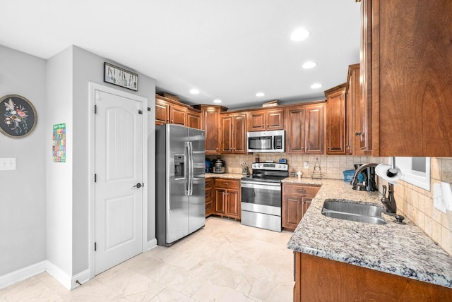 kitchen featuring light stone countertops, appliances with stainless steel finishes, backsplash, and sink