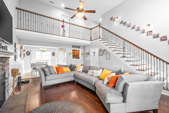 living room with a towering ceiling, a fireplace, ceiling fan, and dark hardwood / wood-style floors