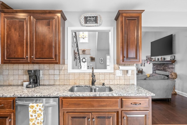 kitchen featuring a stone fireplace, dark hardwood / wood-style flooring, light stone counters, sink, and stainless steel dishwasher