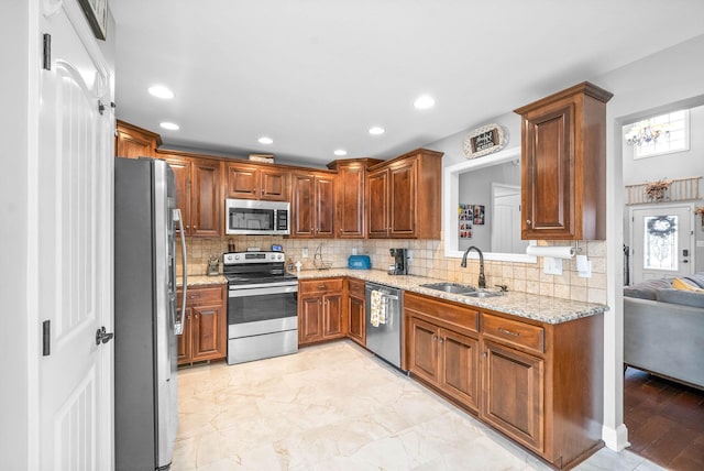 kitchen featuring light stone countertops, a chandelier, stainless steel appliances, tasteful backsplash, and sink