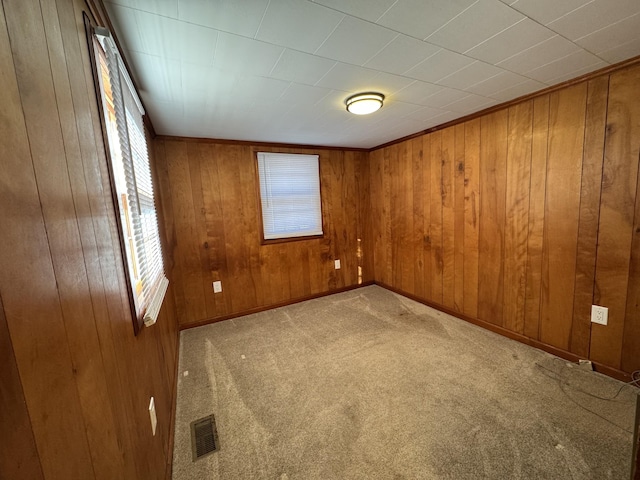 unfurnished room with light carpet, a wealth of natural light, and wooden walls