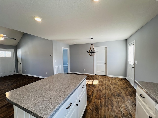 kitchen with dark hardwood / wood-style flooring, ceiling fan with notable chandelier, white cabinets, a center island, and hanging light fixtures