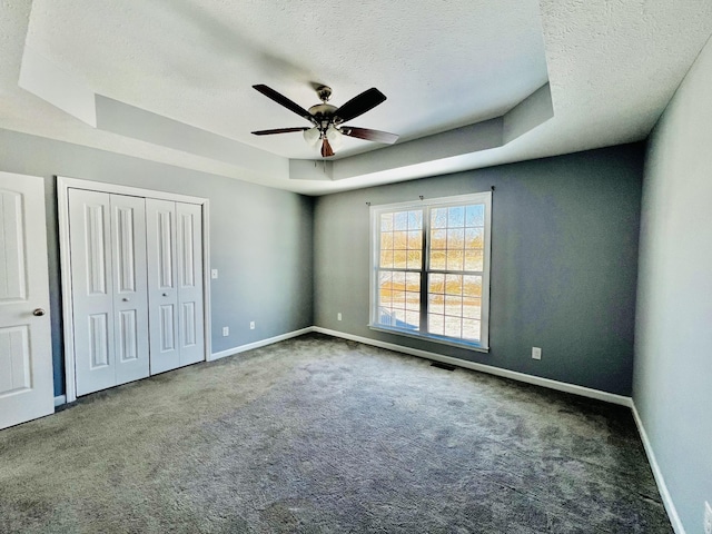 unfurnished bedroom featuring dark colored carpet, a textured ceiling, a tray ceiling, and ceiling fan