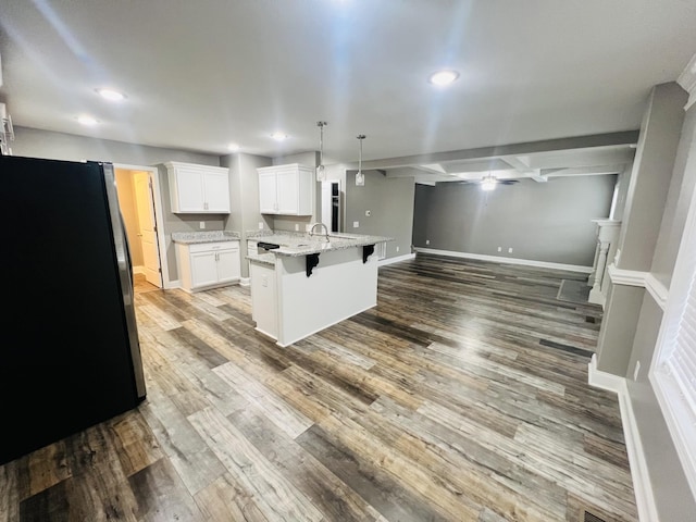 kitchen featuring a breakfast bar, decorative light fixtures, stainless steel fridge, a kitchen island with sink, and white cabinets