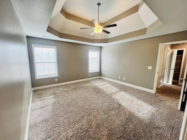 carpeted empty room with a raised ceiling and ceiling fan