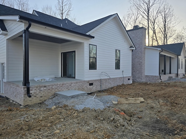 rear view of property with a chimney, roof with shingles, and crawl space