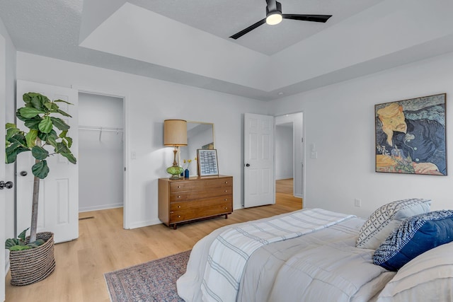 bedroom with a walk in closet, light hardwood / wood-style floors, a closet, ceiling fan, and a tray ceiling