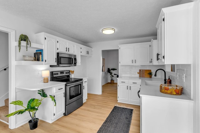 kitchen featuring decorative backsplash, sink, white cabinetry, light hardwood / wood-style flooring, and appliances with stainless steel finishes