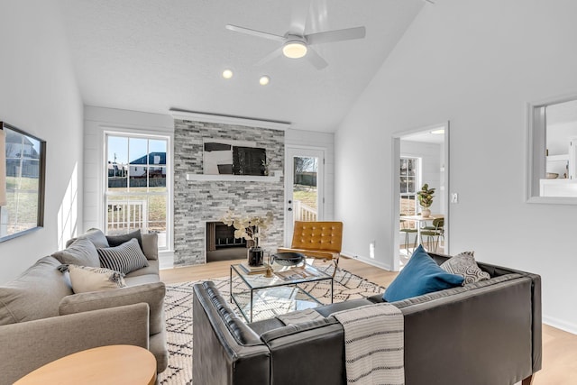 living room featuring a textured ceiling, ceiling fan, light hardwood / wood-style flooring, and a stone fireplace