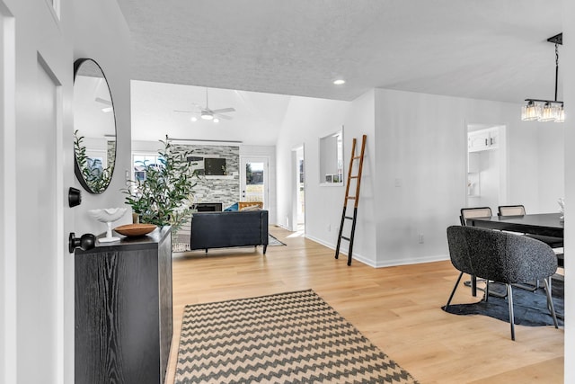 interior space with ceiling fan with notable chandelier, a textured ceiling, hardwood / wood-style floors, lofted ceiling, and a large fireplace