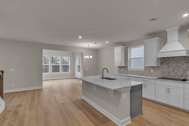 kitchen featuring an island with sink, custom range hood, sink, and white cabinets