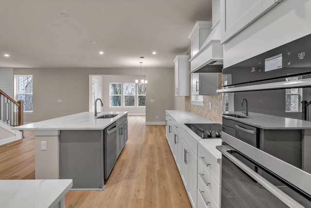 kitchen featuring appliances with stainless steel finishes, decorative light fixtures, sink, white cabinets, and a center island with sink