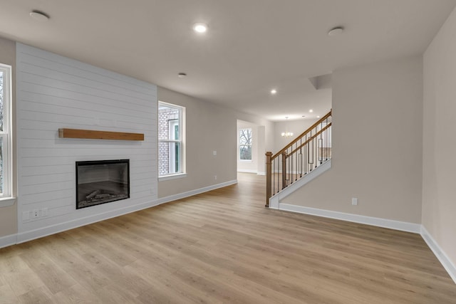 unfurnished living room with a large fireplace, a chandelier, and light hardwood / wood-style flooring