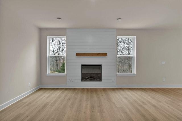 unfurnished living room featuring light hardwood / wood-style flooring, a fireplace, and a healthy amount of sunlight