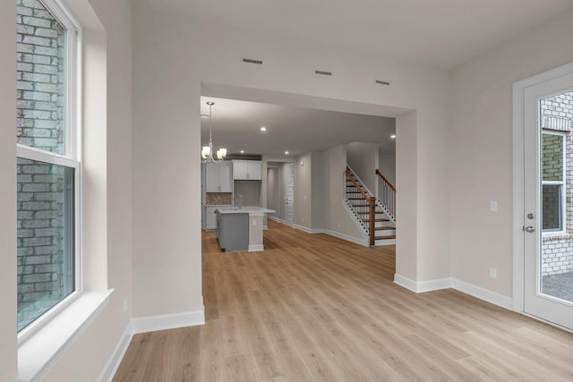 unfurnished living room featuring an inviting chandelier and light hardwood / wood-style flooring