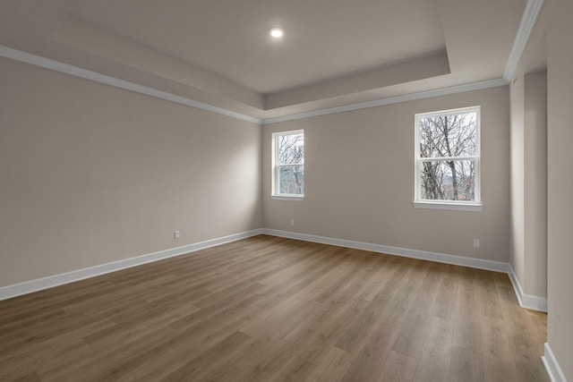 empty room with ornamental molding, a tray ceiling, and light hardwood / wood-style flooring