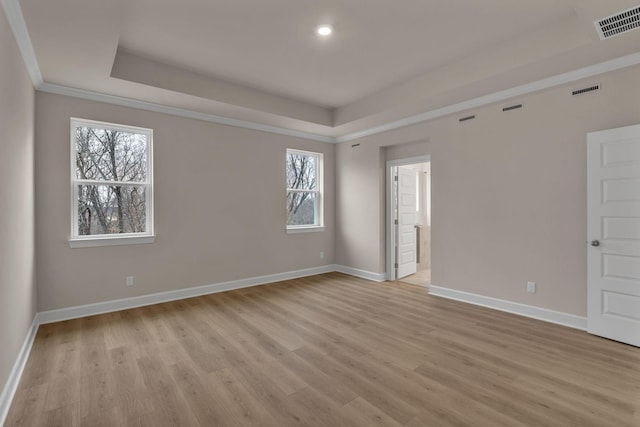 empty room with crown molding, a raised ceiling, and light hardwood / wood-style flooring