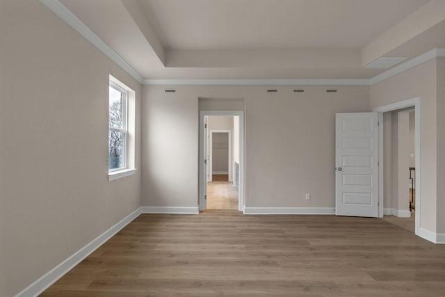 empty room featuring crown molding, light hardwood / wood-style floors, and a tray ceiling