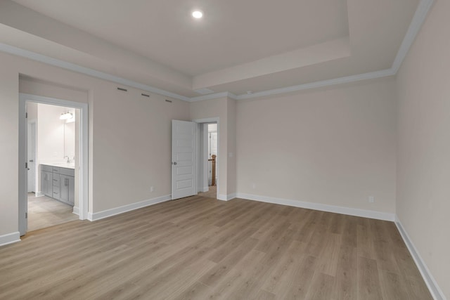 empty room featuring ornamental molding, a raised ceiling, and light wood-type flooring