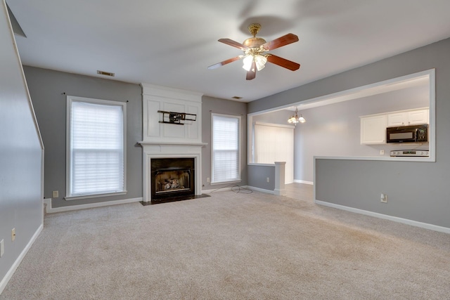 unfurnished living room featuring ceiling fan with notable chandelier, a large fireplace, and light colored carpet