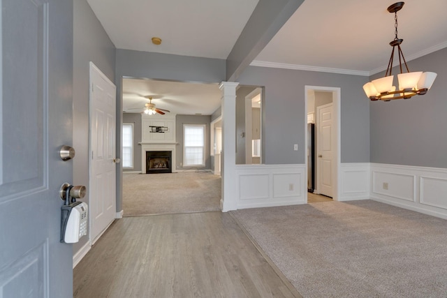 interior space with light carpet, ceiling fan with notable chandelier, ornate columns, and ornamental molding