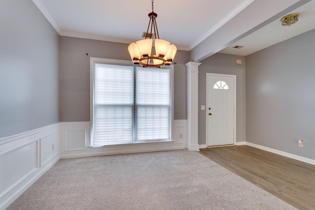 carpeted foyer entrance with plenty of natural light, decorative columns, crown molding, and an inviting chandelier