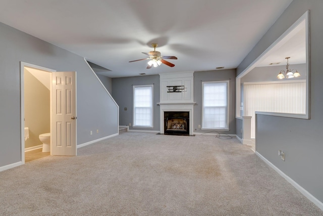 unfurnished living room with ceiling fan with notable chandelier, light carpet, and a large fireplace