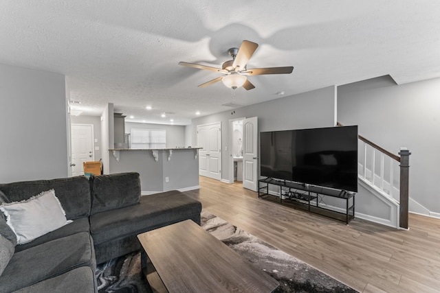 living room featuring ceiling fan, a textured ceiling, and light wood-type flooring