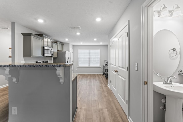 kitchen featuring a kitchen breakfast bar, gray cabinets, a textured ceiling, and appliances with stainless steel finishes