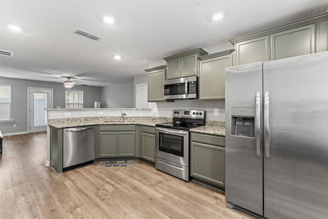 kitchen with ceiling fan, sink, stainless steel appliances, kitchen peninsula, and light wood-type flooring