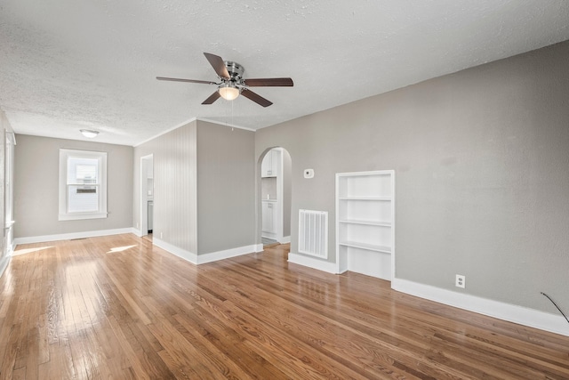 interior space featuring ceiling fan, wood-type flooring, built in features, and a textured ceiling