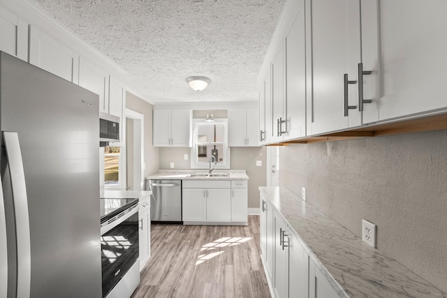 kitchen with sink, light hardwood / wood-style flooring, appliances with stainless steel finishes, a textured ceiling, and white cabinets