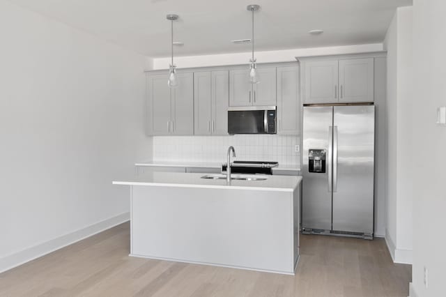 kitchen featuring light hardwood / wood-style flooring, stainless steel appliances, decorative backsplash, a center island with sink, and decorative light fixtures