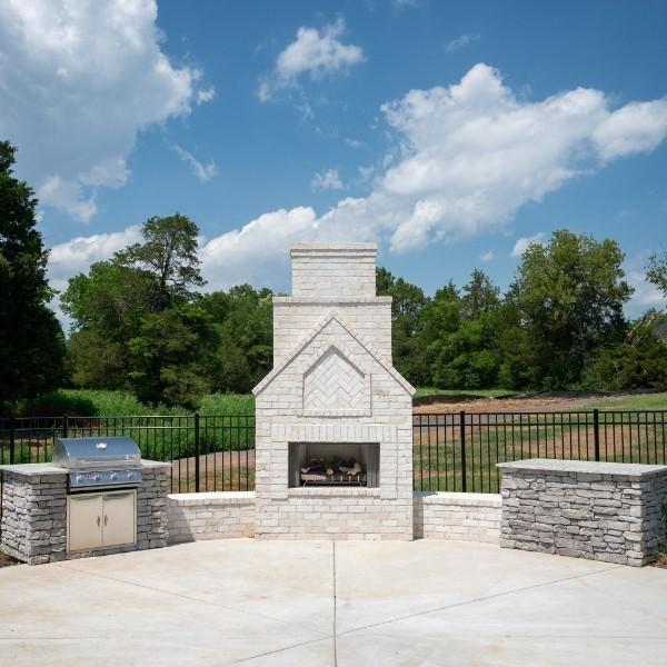 view of patio / terrace featuring an outdoor brick fireplace, fence, grilling area, and an outdoor kitchen