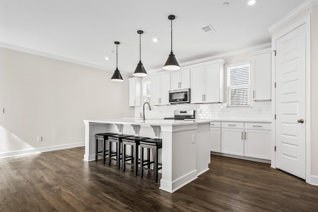 kitchen featuring appliances with stainless steel finishes, a kitchen island with sink, ornamental molding, and visible vents