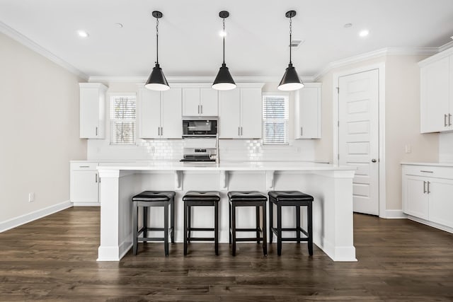 kitchen featuring an island with sink, backsplash, stainless steel appliances, and crown molding