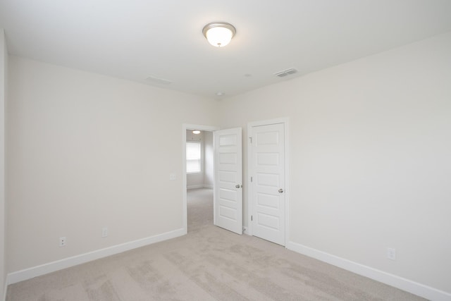 spare room with light colored carpet, visible vents, and baseboards