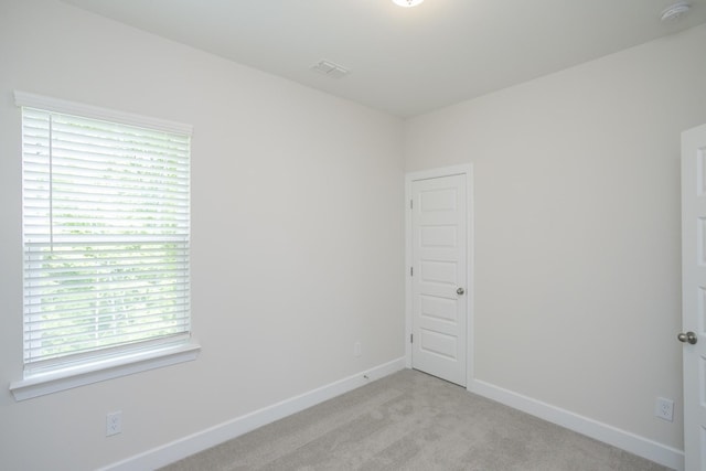 empty room featuring light carpet, visible vents, and baseboards