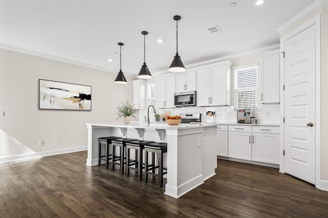 kitchen with a breakfast bar area, stainless steel appliances, a wealth of natural light, an island with sink, and crown molding