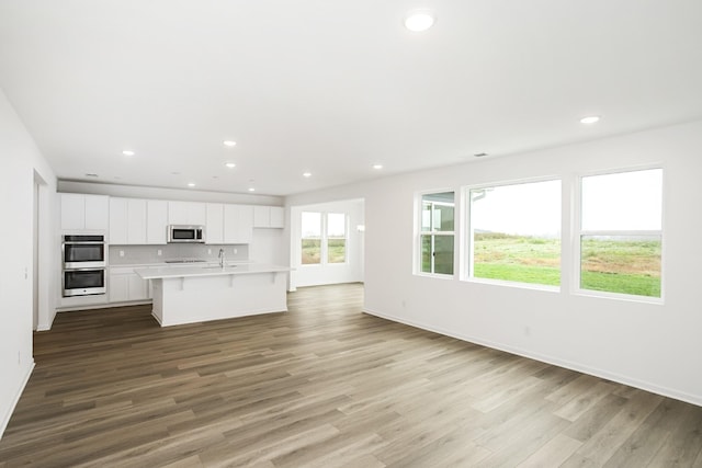 kitchen featuring a kitchen breakfast bar, stainless steel appliances, a center island with sink, white cabinets, and light hardwood / wood-style floors