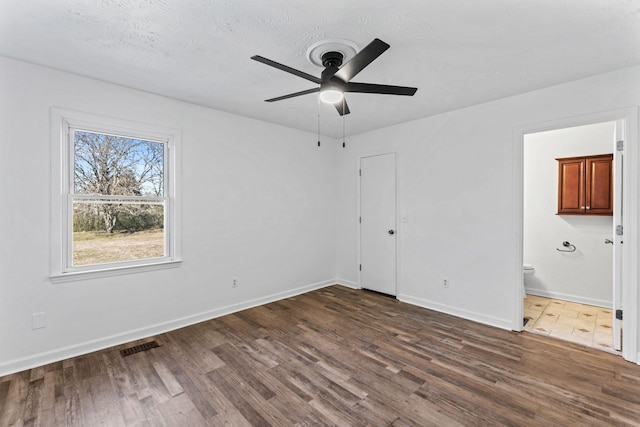 unfurnished bedroom with ceiling fan, dark wood-type flooring, connected bathroom, and a textured ceiling