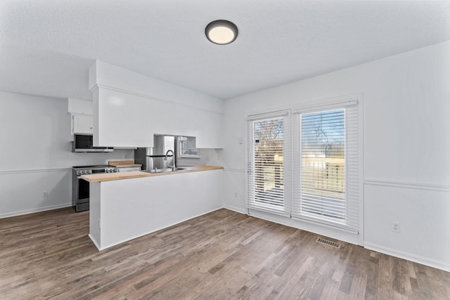 kitchen with dark wood-type flooring, stainless steel appliances, white cabinets, and kitchen peninsula