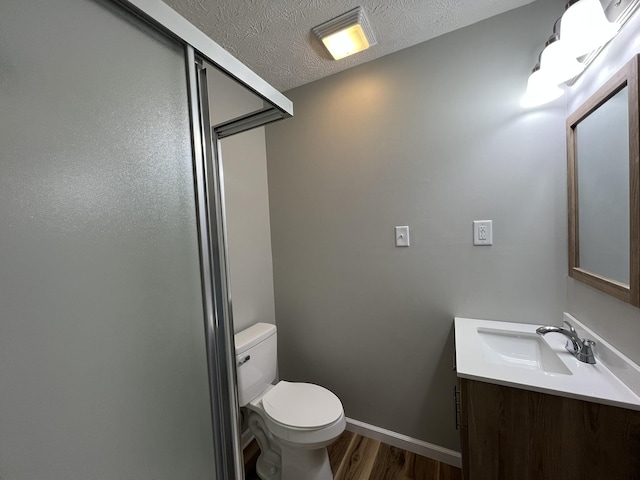 bathroom featuring vanity, hardwood / wood-style flooring, toilet, a textured ceiling, and a shower with shower door