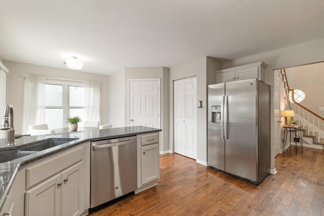 kitchen with stainless steel appliances, sink, dark stone countertops, white cabinets, and dark hardwood / wood-style floors