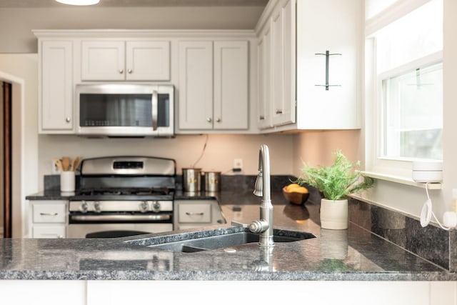 kitchen with white cabinets, sink, stainless steel appliances, and dark stone counters