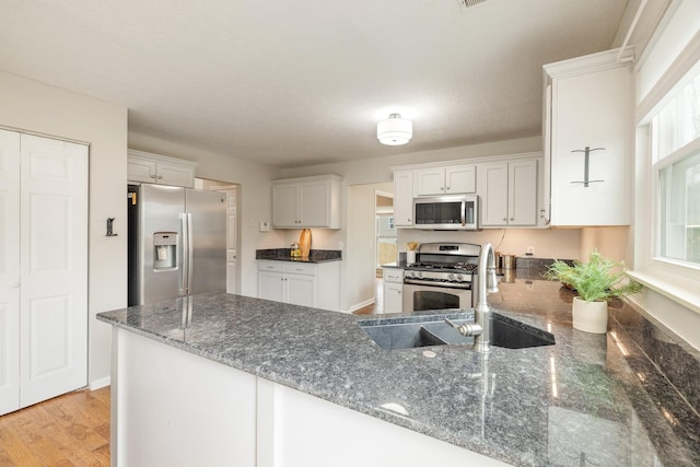 kitchen with sink, stainless steel appliances, kitchen peninsula, dark stone counters, and white cabinets