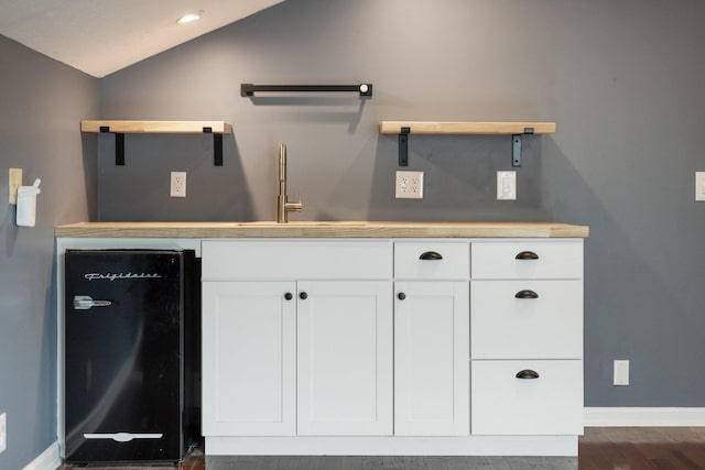 interior space featuring dishwashing machine, sink, dark hardwood / wood-style floors, white cabinetry, and lofted ceiling