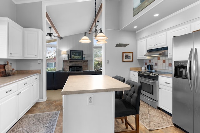 kitchen featuring a kitchen bar, appliances with stainless steel finishes, a fireplace, white cabinets, and a kitchen island