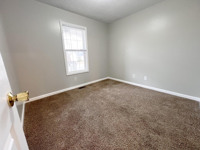 spare room featuring carpet floors, visible vents, baseboards, and a textured ceiling